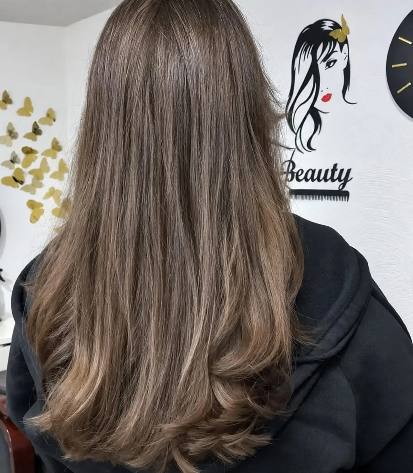 Bruin haar met balayage in laagjes, voor de muur van de salon met een lijntekening en gouden vlinders