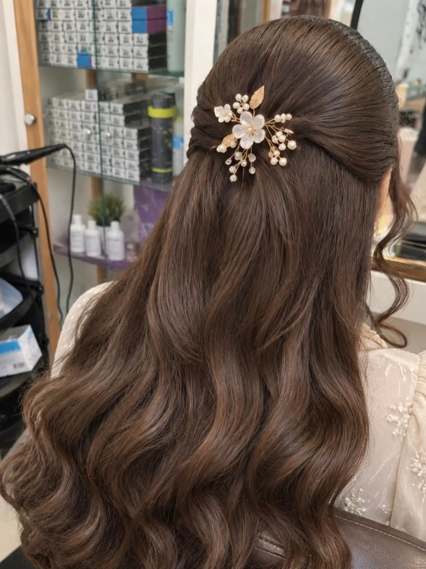 Half opgestoken lang bruin haar in golven, met een gouden bloemenspeld